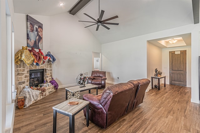 living room with ceiling fan, hardwood / wood-style flooring, a stone fireplace, beam ceiling, and high vaulted ceiling