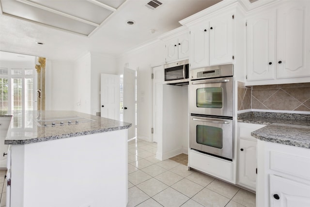 kitchen featuring a kitchen island, appliances with stainless steel finishes, white cabinets, backsplash, and light tile floors