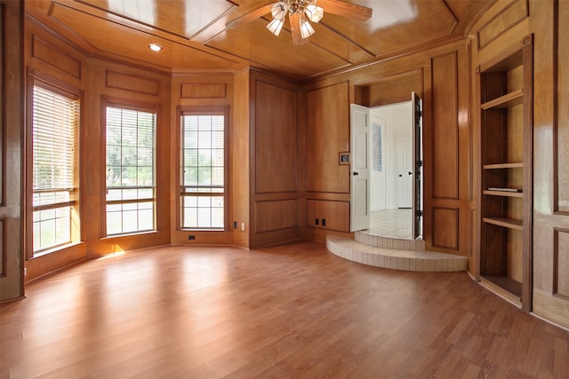 empty room featuring built in features, ceiling fan, wooden walls, and hardwood / wood-style flooring