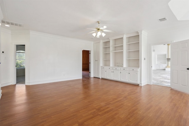 unfurnished living room featuring hardwood / wood-style flooring, built in features, ornamental molding, and ceiling fan