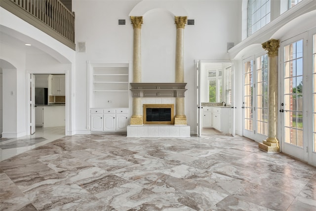 unfurnished living room with a tiled fireplace, french doors, built in shelves, tile floors, and a towering ceiling