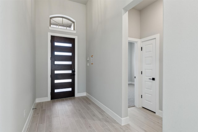 foyer entrance featuring wood finish floors, a towering ceiling, and baseboards