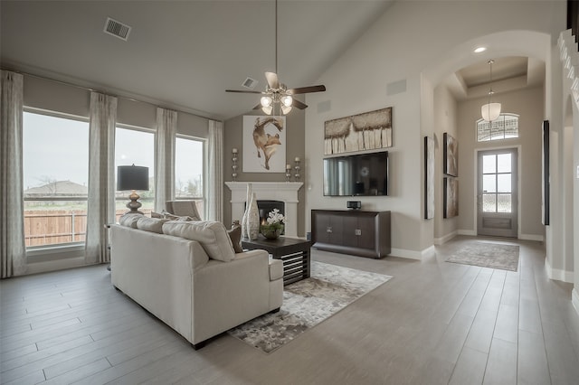 living room with ceiling fan, light hardwood / wood-style flooring, a towering ceiling, and a healthy amount of sunlight