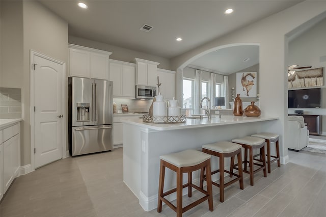 kitchen featuring decorative backsplash, a kitchen bar, stainless steel appliances, sink, and white cabinets