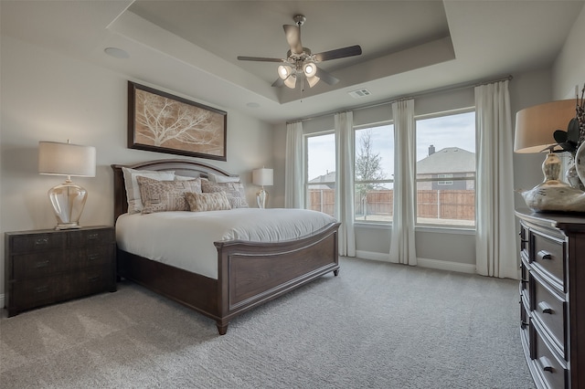 carpeted bedroom with ceiling fan and a tray ceiling