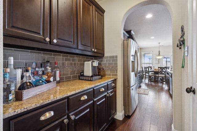 kitchen with stainless steel fridge, decorative light fixtures, dark wood-type flooring, dark brown cabinetry, and backsplash