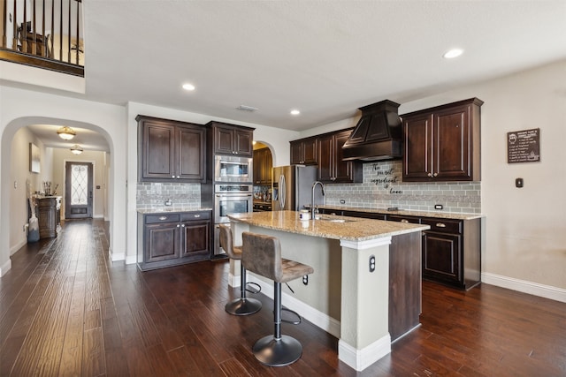 kitchen featuring custom range hood, stainless steel appliances, a center island with sink, dark wood-type flooring, and sink