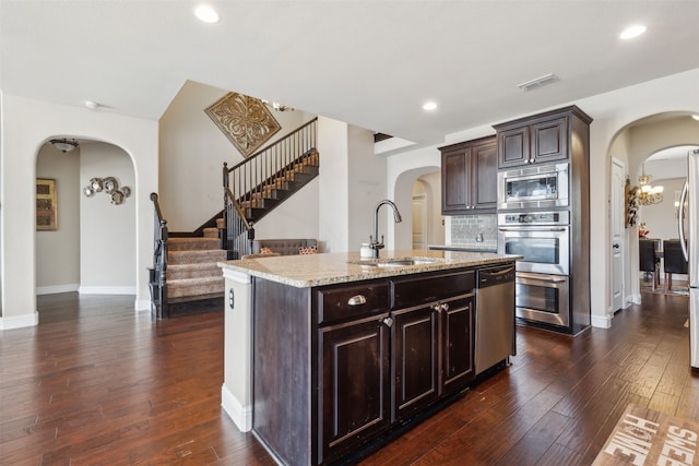 kitchen with dark hardwood / wood-style flooring, backsplash, an island with sink, sink, and appliances with stainless steel finishes