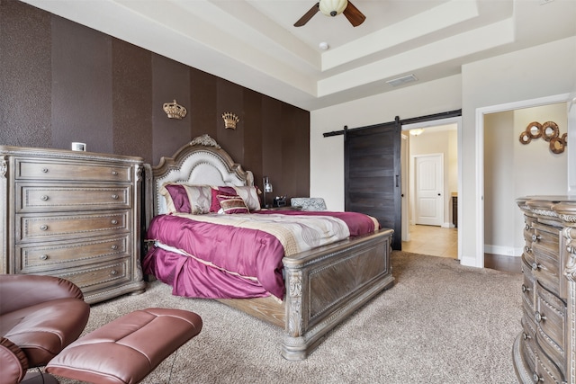 bedroom featuring a barn door, ceiling fan, a tray ceiling, and light tile flooring