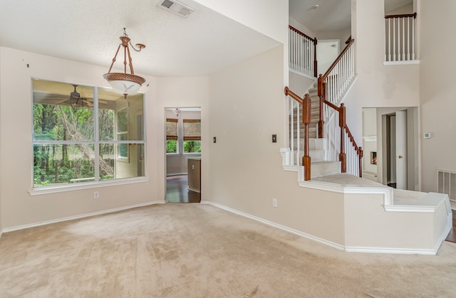 carpeted spare room featuring a towering ceiling and ceiling fan