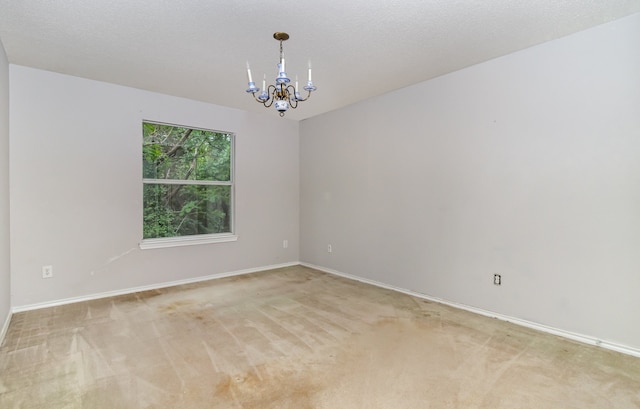 unfurnished room with an inviting chandelier, a textured ceiling, and carpet flooring