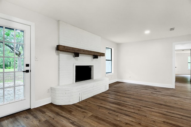 unfurnished living room featuring dark hardwood / wood-style floors, brick wall, a wealth of natural light, and a brick fireplace