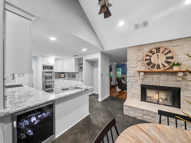 kitchen featuring wine cooler, light stone counters, vaulted ceiling, sink, and white cabinetry