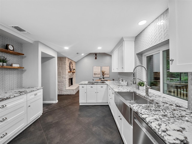 kitchen with sink, kitchen peninsula, light stone countertops, a fireplace, and white cabinetry