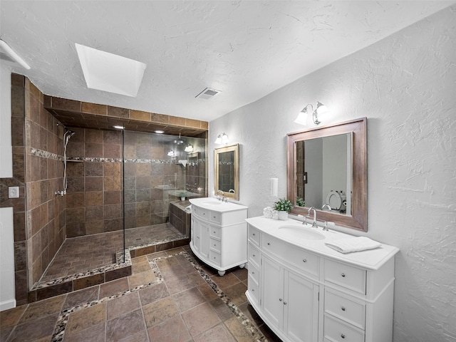 bathroom with a skylight, vanity, a textured ceiling, and tiled shower