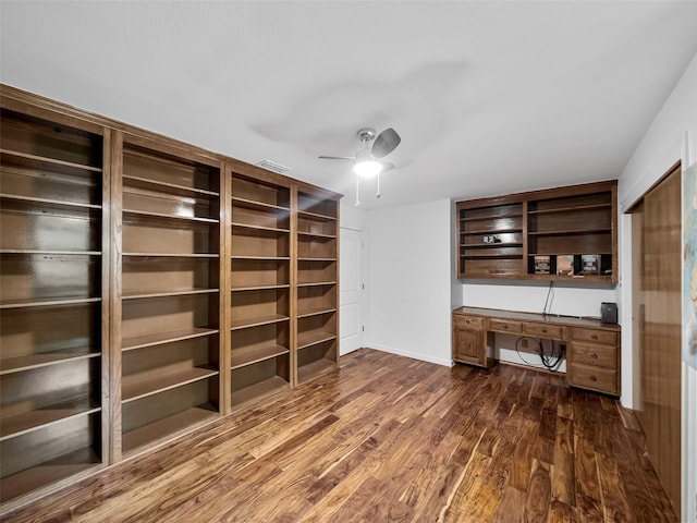 unfurnished office featuring built in desk, dark hardwood / wood-style floors, and ceiling fan