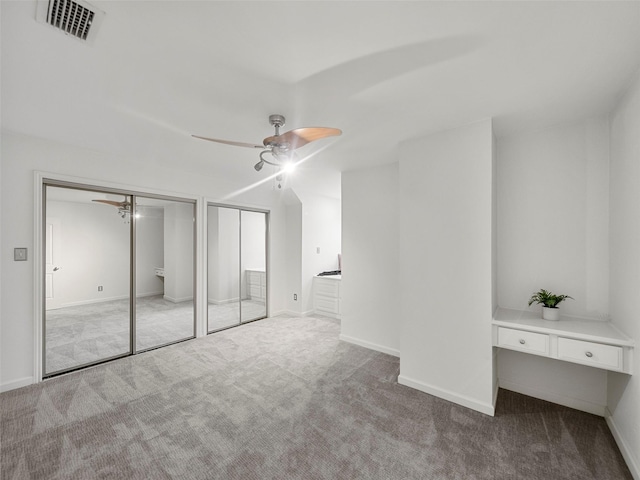 unfurnished bedroom featuring multiple closets, ceiling fan, and light colored carpet