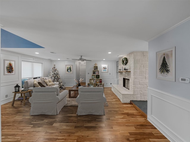 living room featuring hardwood / wood-style floors, ceiling fan, ornamental molding, and a fireplace