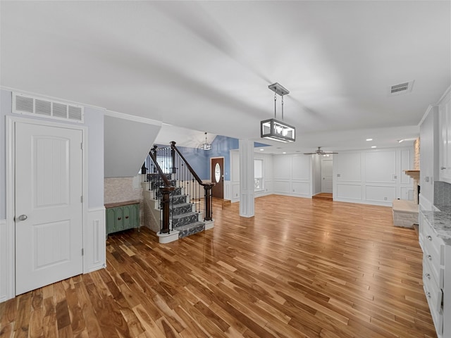 unfurnished living room with crown molding, wood-type flooring, and ceiling fan with notable chandelier