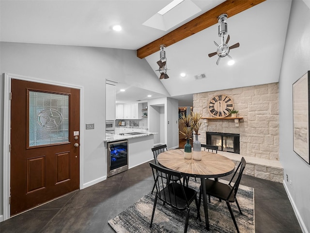 dining space with vaulted ceiling with beams, ceiling fan, a stone fireplace, and beverage cooler