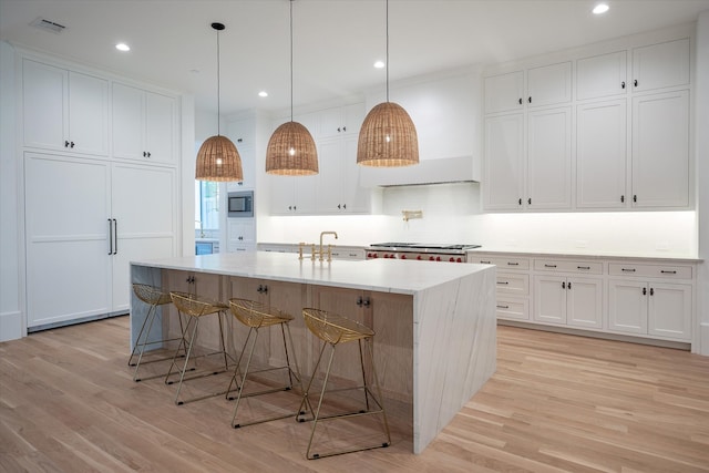 kitchen featuring decorative light fixtures, a kitchen island with sink, light hardwood / wood-style flooring, white cabinetry, and stainless steel appliances