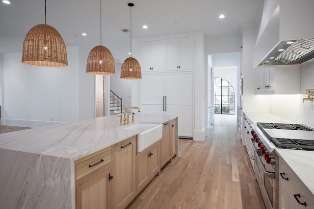 kitchen featuring pendant lighting, sink, light hardwood / wood-style flooring, wall chimney range hood, and a spacious island