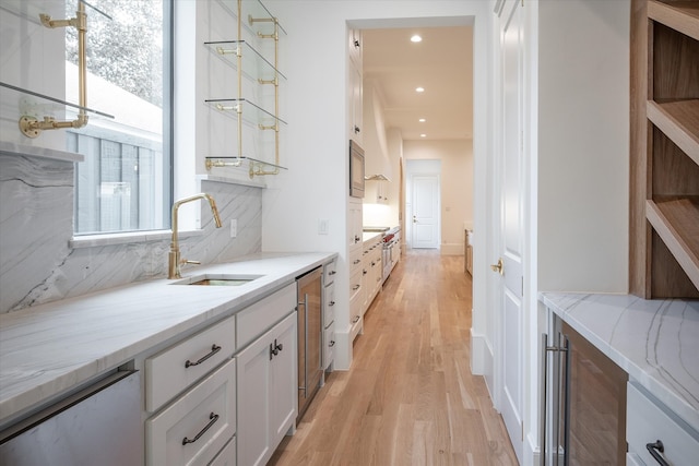 kitchen featuring light hardwood / wood-style floors, sink, white cabinetry, decorative backsplash, and light stone countertops