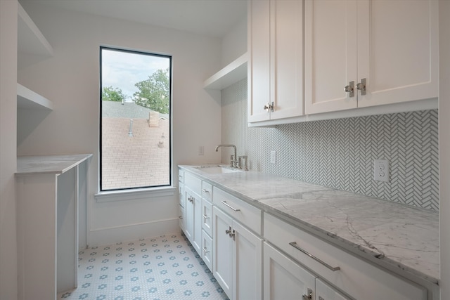 kitchen with light stone countertops, backsplash, sink, and white cabinetry