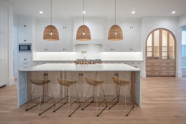 kitchen featuring a large island, white cabinetry, built in microwave, and a breakfast bar area