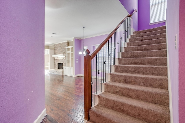 staircase with a stone fireplace, ornamental molding, hardwood / wood-style flooring, and a chandelier