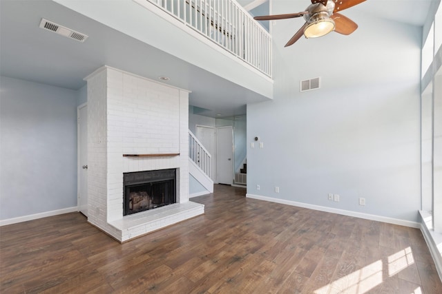 unfurnished living room with a towering ceiling, dark hardwood / wood-style floors, a brick fireplace, and ceiling fan