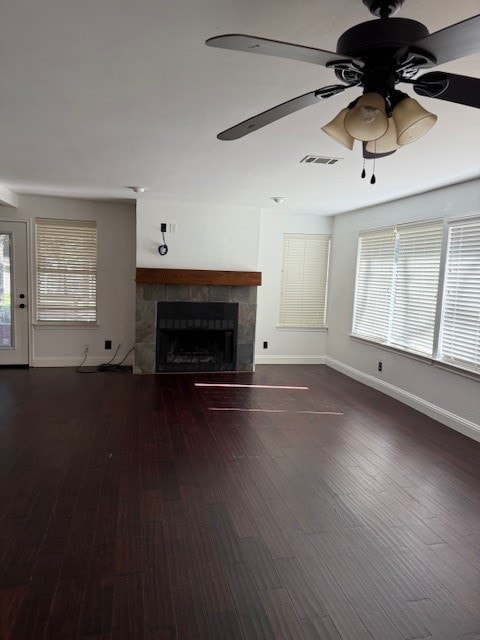 unfurnished living room with dark hardwood / wood-style floors, ceiling fan, a tile fireplace, and a wealth of natural light