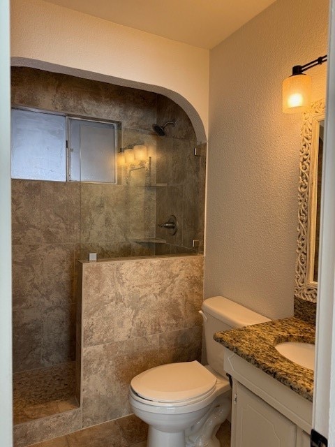 bathroom featuring tiled shower, vanity, toilet, and tile patterned flooring