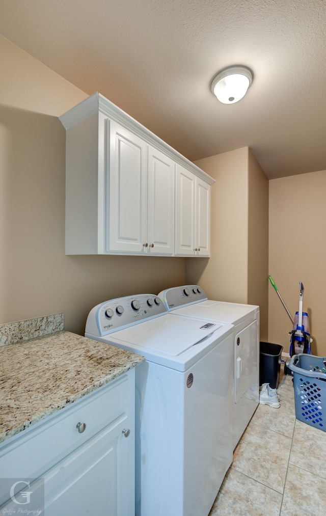 clothes washing area featuring washing machine and clothes dryer, cabinets, and light tile floors