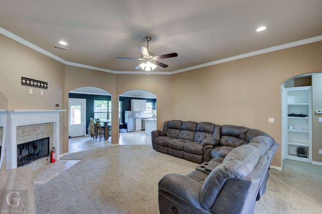 carpeted living room with a tiled fireplace, ceiling fan, and ornamental molding