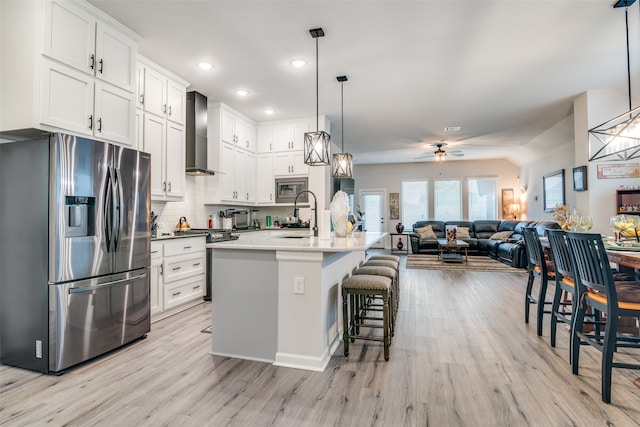 kitchen featuring light hardwood / wood-style floors, a kitchen breakfast bar, ceiling fan, wall chimney exhaust hood, and appliances with stainless steel finishes