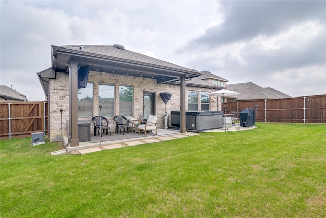 back of house featuring a hot tub, a patio area, and a lawn