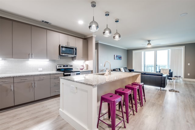 kitchen with light stone countertops, a center island with sink, light hardwood / wood-style flooring, stainless steel appliances, and decorative light fixtures