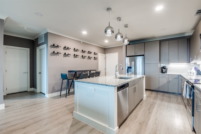 kitchen featuring light hardwood / wood-style floors, hanging light fixtures, a center island with sink, appliances with stainless steel finishes, and tasteful backsplash