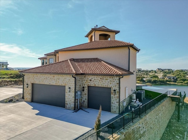 view of side of home with fence, concrete driveway, a garage, and stone siding