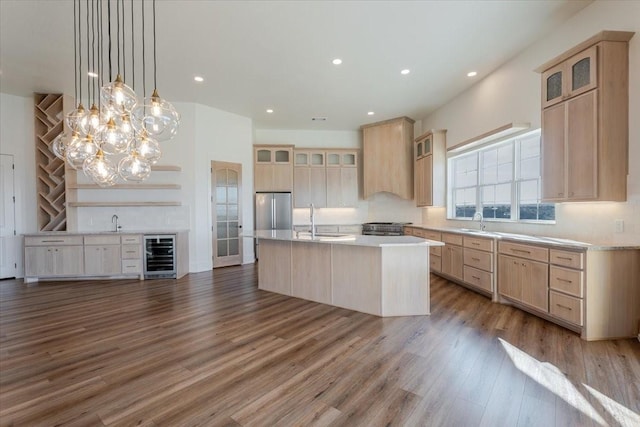 kitchen with appliances with stainless steel finishes, decorative light fixtures, wine cooler, light brown cabinets, and a kitchen island with sink