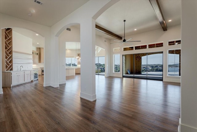 unfurnished living room featuring a ceiling fan, dark wood finished floors, and beamed ceiling