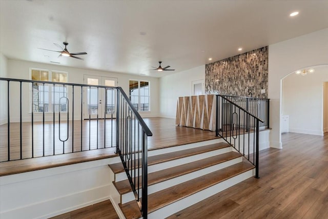 stairs featuring baseboards, arched walkways, ceiling fan, and wood finished floors