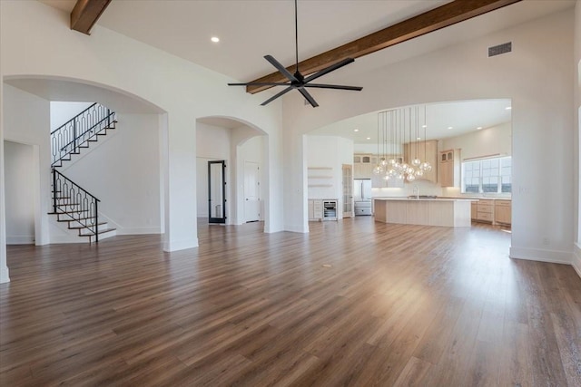 unfurnished living room featuring beam ceiling, high vaulted ceiling, dark wood finished floors, ceiling fan with notable chandelier, and visible vents