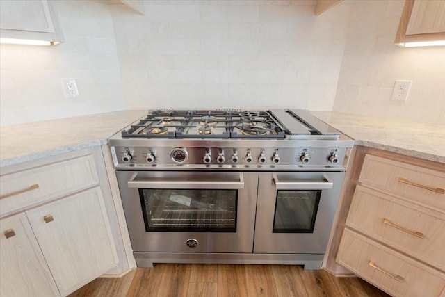 kitchen featuring light brown cabinetry, tasteful backsplash, double oven range, and light stone counters