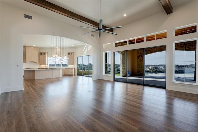 unfurnished living room featuring ceiling fan with notable chandelier, a healthy amount of sunlight, dark hardwood / wood-style flooring, and beam ceiling