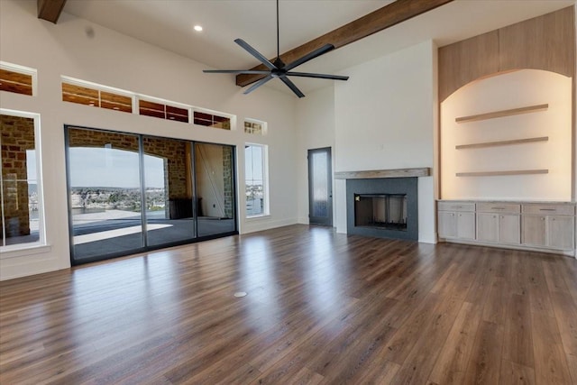 unfurnished living room with a ceiling fan, a towering ceiling, a fireplace, beam ceiling, and wood finished floors