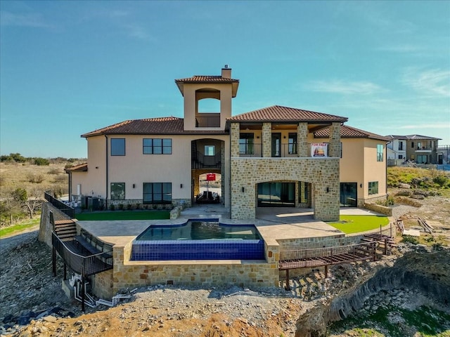 back of property featuring a chimney, a patio area, stone siding, and a balcony