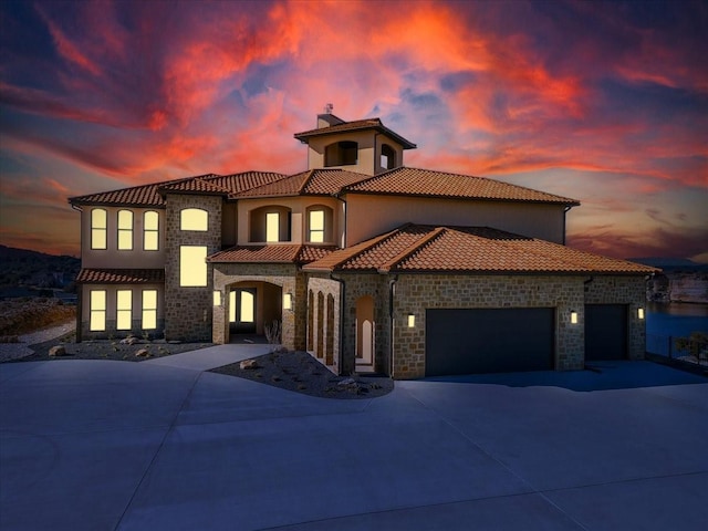 mediterranean / spanish-style home with an attached garage, stone siding, a chimney, a tiled roof, and driveway