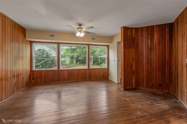 unfurnished room featuring ceiling fan, dark hardwood / wood-style flooring, and wooden walls